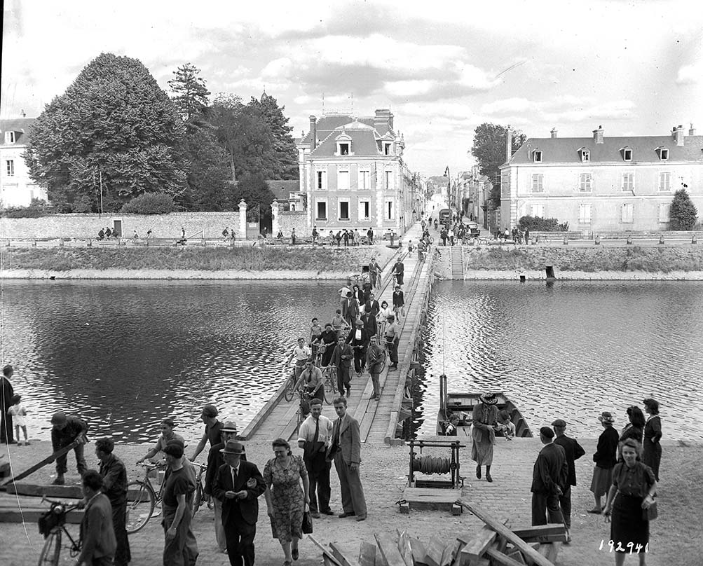 Civils franchissant la Mayenne sur un pont de bois construit par l'armée américaine dans le prolongement de la rue Crossardière le 18 août 1944.